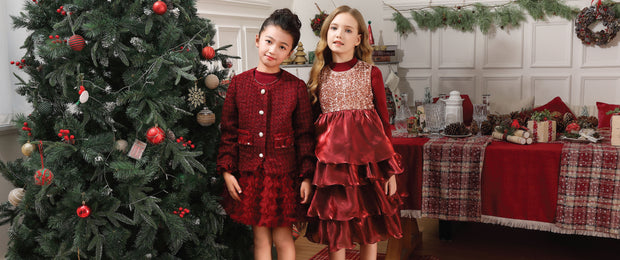 Tulleen Two children in red dresses standing next to a decorated Christmas tree in a festive room.