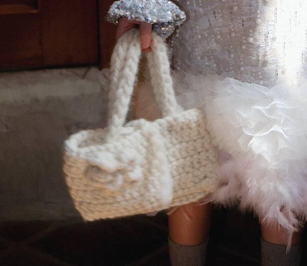 Girl in sparkly Tulleen holiday outfit holding chunky knit handbag, styled in cozy-glam textures