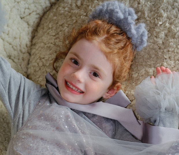 Smiling child in sparkly silver Tulleen holiday dress with tulle and headband, lying playfully on plush rug.