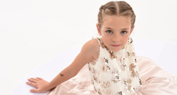 Young girl wearing a white dress with floral embellishments on a white background