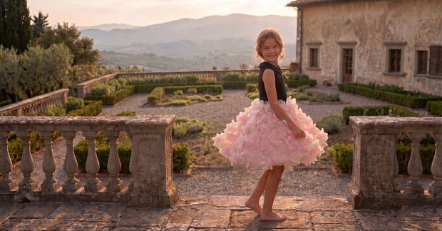 Young girl in black top and pink ruffled skirt on a villa terrace.